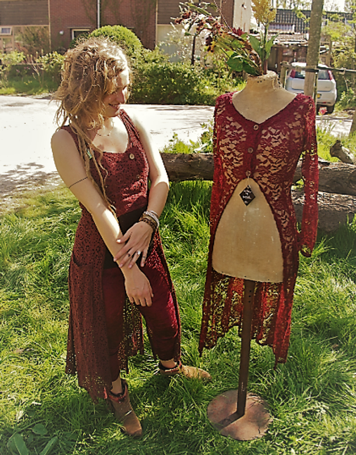 Marie, the designer, standing beside a mannequin displaying a red lace dress in an outdoor setting.